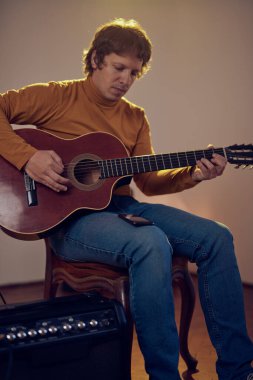 Erkek müzisyen retro vintage odasındaki amplifikatörde akustik gitar çalıyor..