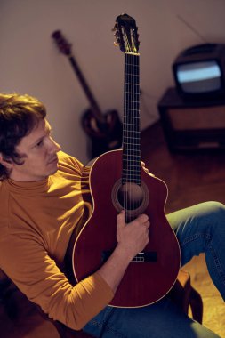 Erkek müzisyen retro vintage odasındaki amplifikatörde akustik gitar çalıyor..