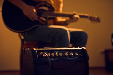Male musician playing acoustic guitar on the amplifier in retro vintage room. clipart
