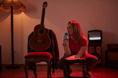 Eski moda bir odada kablosuz bir mikrofonda şarkı söyleyen ve müzik çalan bir kadın..