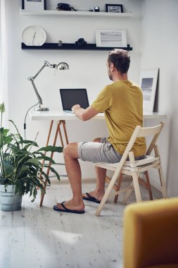Yetişkin beyaz bir adam evde dizüstü bilgisayarla çalışıyor..