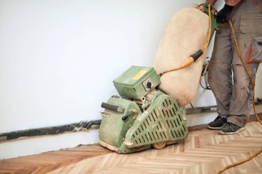 Tamirci zımpara makinesiyle parke onarıyor..