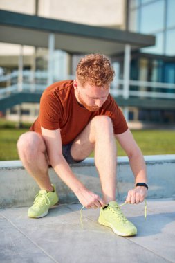 Koşu ayakkabıları bağlayan ve şehir parkında egzersiz yapan genç adam..