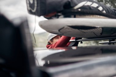 Rüzgâr sörfçüsü ve kampçı, doğada bir arabanın çatı rafından bavulları hazırlayıp boşaltıyorlar..