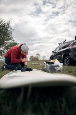 Rüzgâr sörfçüsü ve kampçı, doğada bir arabanın çatı rafından bavulları hazırlayıp boşaltıyorlar..