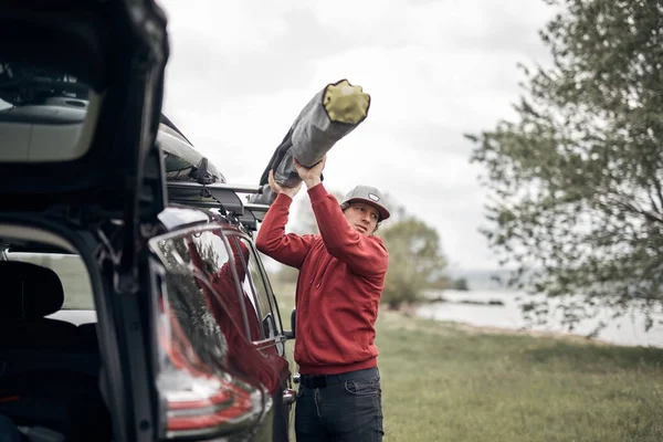 Windsurfer and camper packing and unpacking from a car\'s roof rack in nature.