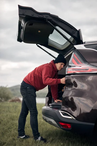 Camper packing and unpacking from a car\'s back door in nature.