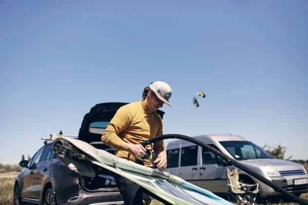 Windsurfer and camper packing and unpacking from a car\'s roof rack in nature.