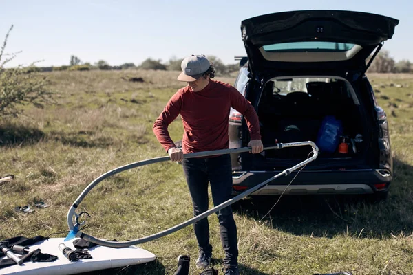 Windsurfer and camper packing and unpacking from a car in nature.