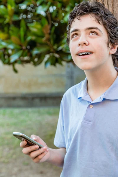boy with braces smiles looking up while using mobile phone