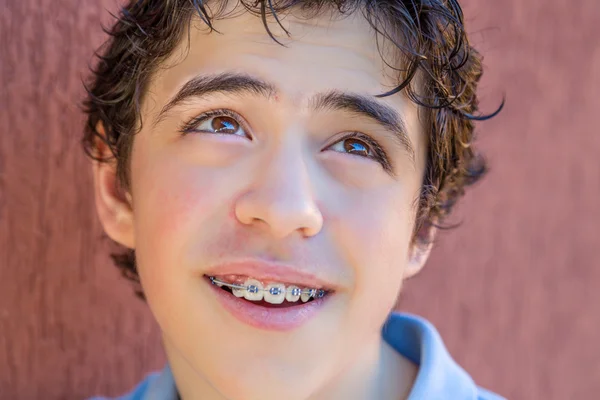 young boy smiling with braces while looking to his top left side