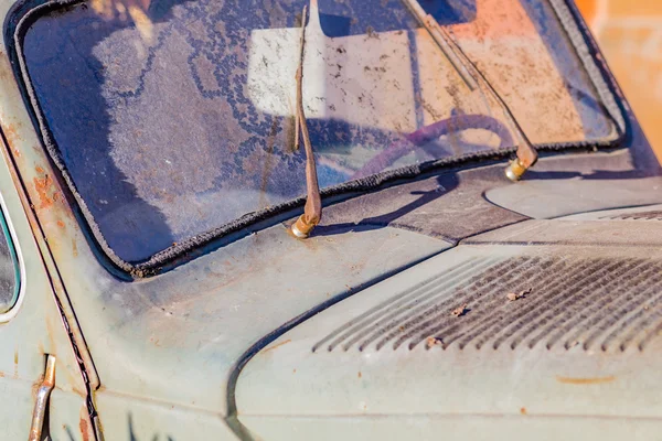 carcass of an old rusty car in the desert sand surrounded by rocks and cactus
