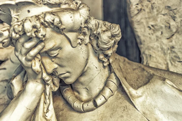 dusted statue of crying angel holding his head while tears is flowing on nose