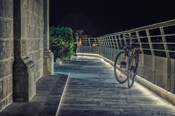 bicycle leaning against a lit railing in front of an old church at night