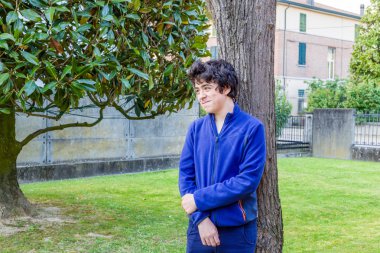 genç çocuk bahçede bir catalpa ağacının gövdesine yaslanmış gülümsüyor