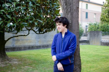 genç çocuk bahçede bir catalpa ağacının gövdesine yaslanmış gülümsüyor