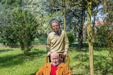 baba ve oğul, yaşlı adam bir sandalyede oturan ve orta yaşlı adam birlikte bahçede