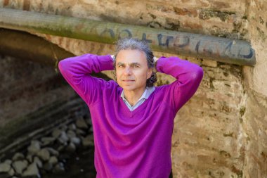 eski bir su kanalının duvarlarının yanında orta yaşlı bir adam başının arkasında ellerini geçerken