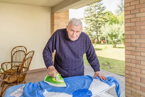 Senior ironing in the patio of his house