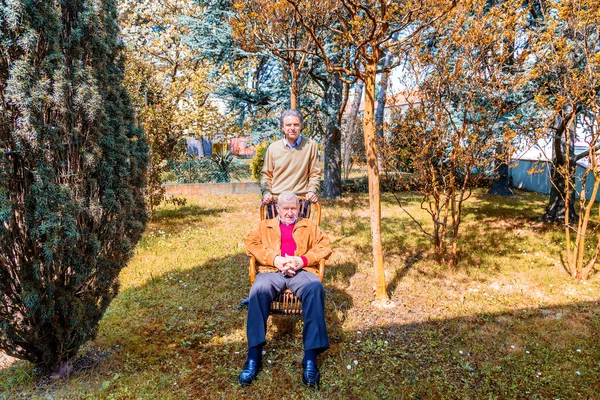 father and son, Elderly man sitting on a chair and middle-aged man together in the garden