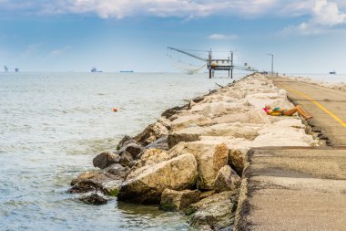 kadın dalgakıran kayalar üzerinde güneşlenirken iskelede balıkçılar ve balıkçı kulübesi