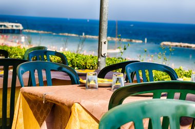 Plaj ve deniz panoraması ile kağıt masa örtüsü ve gözlük yüklü plastik bir masadan görünümü