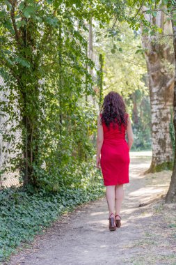 arka görünümü kadının kırmızı, yüksek topuklar ve ağaçları arasında bir yol içine girişimler kokteyl elbisesi