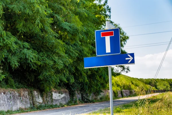 dead end road and direction sign to the right, both without written words, situated on a country road near the bank of a river