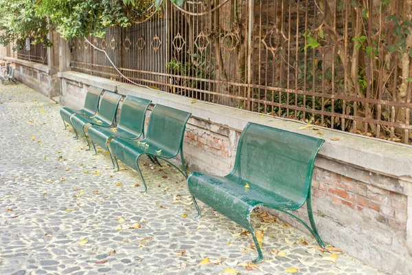 葉と花粉のある石畳の通りに並ぶ緑色の鉄のベンチ — ストック写真