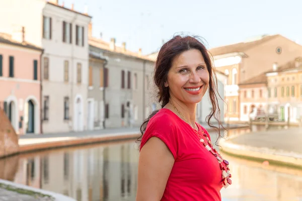 地中海成熟妇女穿着红色礼服沿着意大利一个古老村庄的运河行走的环境肖像 被称为小威尼斯 — 图库照片