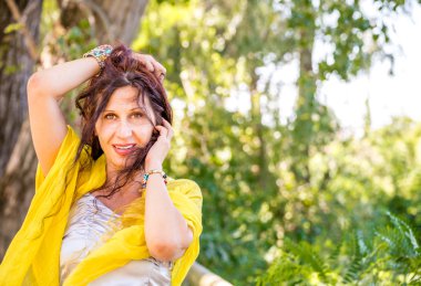 sarı şal ve gümüş üst ile zarif ve çekici olgun kadın saç ile oynarken yeşil bir parkta gülümsüyor