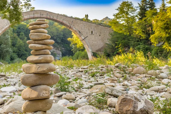 pile of stones in front of 500 years old hunchback Renaissance bridge connecting two banks with single span in Italian Countryside