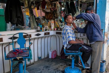Imphal, Hindistan - Aralık 2020: Berber dükkanında maske takmış bir berber 30 Aralık 2020 'de Imphal, Manipur, Hindistan' da bir müşterisini tıraş ediyor.