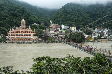 Rishikesh, Hindistan - Temmuz 2021: 20 Temmuz 2021 'de Uttarakhand, Hindistan' da bulunan Swarg Niwa Tapınağının yanındaki Lakshman Jhula Köprüsü 'nden geçenler.