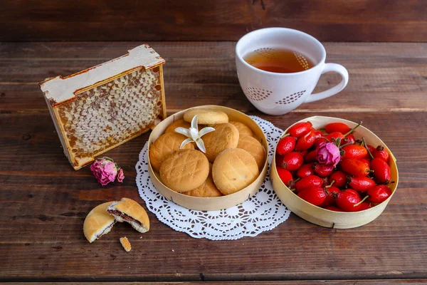 Still life with rose hips, tea, honeycombs and cookies on a wooden background
