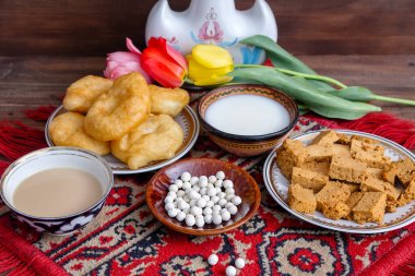 Kazakh still life on Nauryz, with national food: baursaks, irimshik, kurt, koumiss and tea on a wooden background clipart