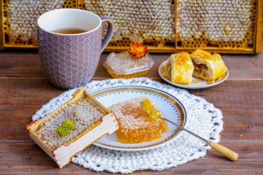 Rustic still life with beekeeping products: honey combs in a glass jar, wild honey in a honeycomb frame on a birch branch, a cookies and cut combs on a plate, on a wooden background clipart