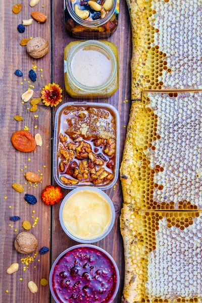 養蜂製品との素朴な静物画 ガラス瓶の中の蜂蜜の櫛 白樺の枝のハニカムフレームの野生の蜂蜜 ラズベリージャム 蜂蜜のスフレ ドライフルーツやナッツ 木製の背景に — ストック写真