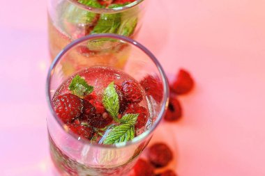 Kırmızı ahududu ve yeşil yapraklı ferahlatıcı bir yaz kokteyli pembe arka planda duruyor. Yakınlarda böğürtlen var. Üst görünüm