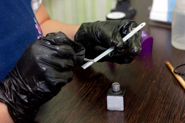 a manicurist in vinyl gloves applies gel polish to a plastic nail tip, creates a sample for a manicure