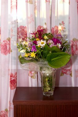 İçinde şakayık, akuleji ve büyük yeşil yapraklar olan büyük, renkli kır çiçekleri. İç kısımdaki bir vazoda tatil için bir hediye.