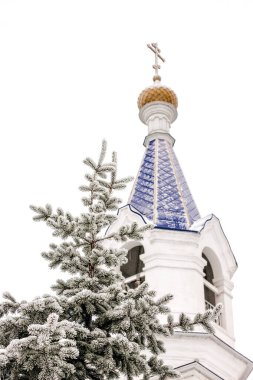 Kış manzarası, çan kulesi ve altın kubbesi olan güzel beyaz tapınak ve donmakta olan altın haç, beyaz gökyüzü ve karın arka planında.