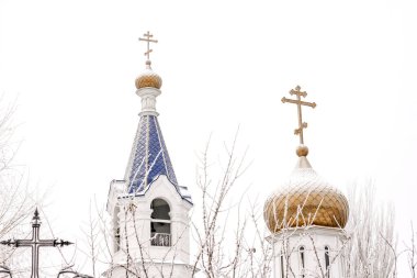 Kış manzarası, çan kulesi ve altın kubbesi olan güzel beyaz tapınak ve donmakta olan altın haç, beyaz gökyüzü ve karın arka planında.