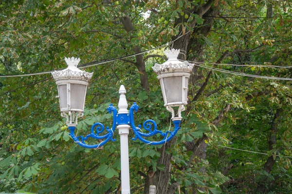 Beautiful decorative street lamp, green leaves and trees background, antique garden or park lamp post