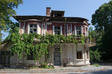 8 Ağustos 2020, selo Qgoda, Bulgaristan - Yeşil bitkilerle kaplı terk edilmiş köy evi, kırık pencere, sokaktaki eski bir evde hasar