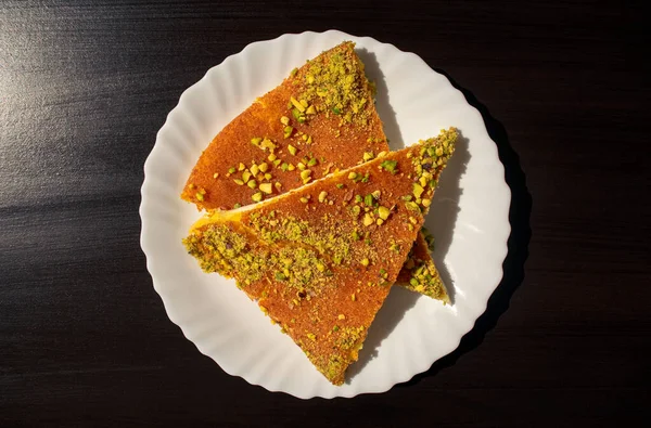 Kunafa-Scheiben vom östlichen Dessert auf einem weißen Teller auf dunkelschwarzem Hintergrund. Ansicht von oben. Arabischer Käse Kunafa auf dunklem. — Stockfoto