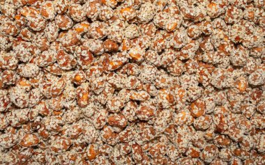 Background made of peanuts or raisins covered with brown caramel and sesame seeds. Carameled nuts