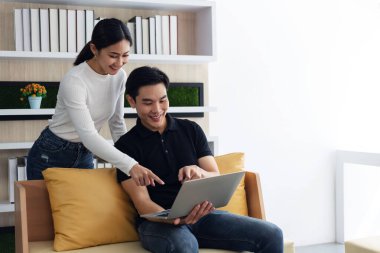 Genç Asyalı kadın ve erkek evdeki dizüstü bilgisayarı işaret ediyorlar.