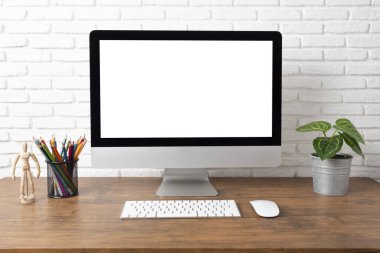 Boş beyaz ekranlı bilgisayar ve ahşap bir masada ofis malzemeleri olan çalışma alanı.
