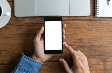 Üst düzey iş adamı elinde boş beyaz ekranlı akıllı telefon ve ahşap masada bilgisayar bilgisayarı tutuyor. 